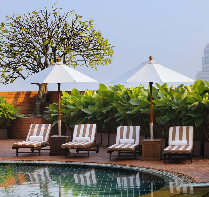 Swimming pool striped chairs and umbrellas plants in the back